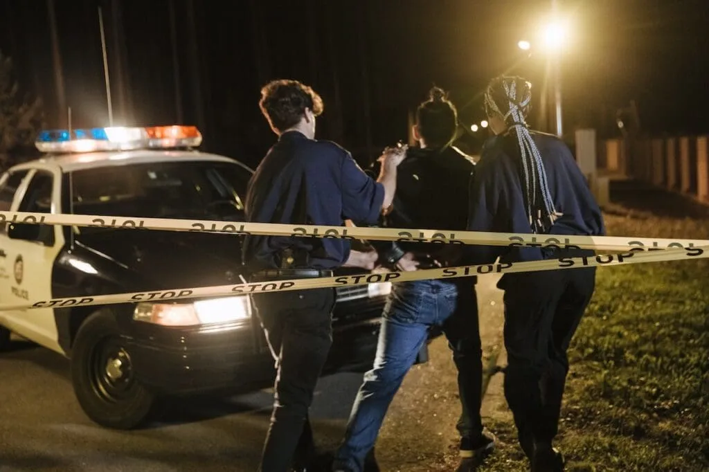 Police arresting a suspect near a police car, highlighting the need for a criminal defense attorney.